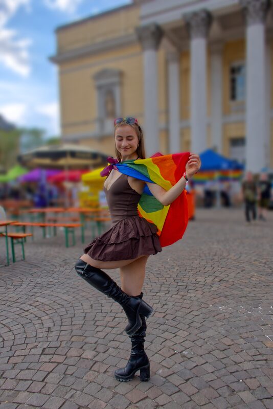Person tanzt mit einer Regenbogenfahne über den Festplatz