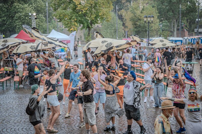 Menschen tanzen zwischen Biertischen und Sonnenschirmen auf dem Festplatz