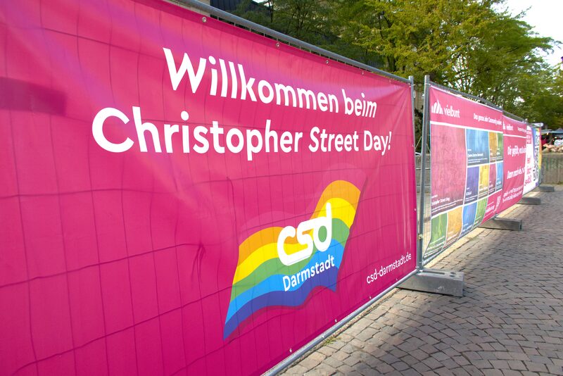 Pinkes Banner am Bauzaun mit der Aufschrift Willkommen beim Christopher Street Day