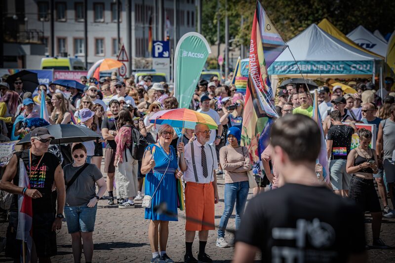 Publikum mit Sonnenschirmen und Fahnen vor der Bühne am Karolinenplatz